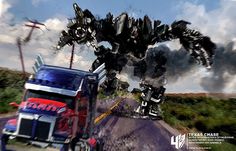 a truck driving down a road next to a giant robot like creature in the sky