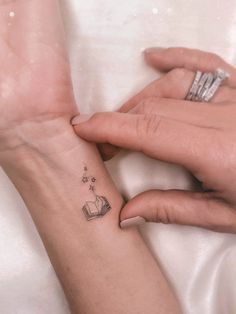 two hands holding each other with small tattoos on their wrist and the one has an open book