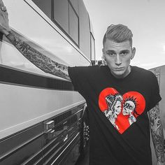 a man standing next to a bus with tattoos on his arms and shoulder, wearing a heart shaped t - shirt