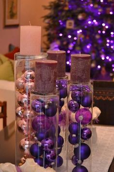 two candles are sitting on a table with purple ornaments in front of a christmas tree