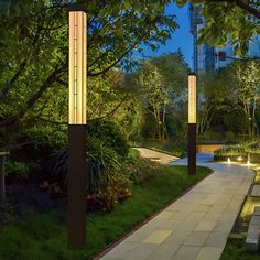 the walkway is lit up at night with lights in the trees and bushes on both sides