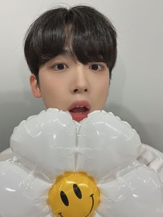 a young man holding up a balloon shaped like a flower with a smiley face on it