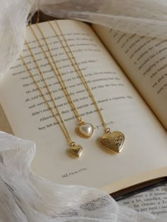 three necklaces are sitting on top of an open book, one with a heart and the other with a pearl