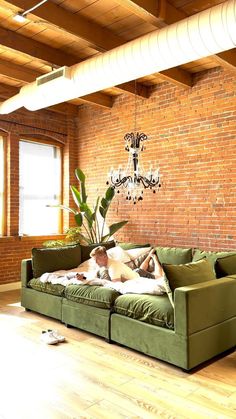 a green couch sitting in front of a brick wall with a chandelier hanging from the ceiling