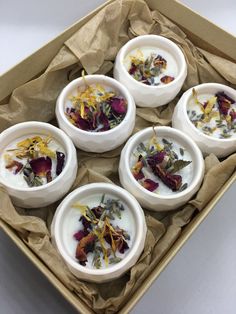 four white bowls filled with different types of flowers on top of brown paper in a box