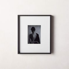 a black and white photo of a woman with her back turned to the camera, framed on a wall