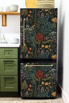 an old fashioned refrigerator is painted with flowers and plants on it's side, next to a green cabinet