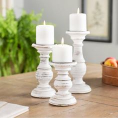 three white candles sitting on top of a wooden table next to apples and oranges