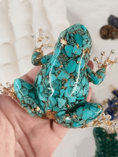 a hand holding a turquoise frog brooch with gold accents on it's body