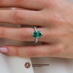 a woman's hand wearing a ring with a green stone in the center and diamond band