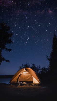 a tent is lit up at night with the stars in the sky and trees around it