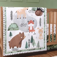 a baby crib bedding set with animals and trees on the wall behind it