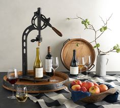 an assortment of wine bottles and glasses on a table next to two wooden trays filled with fruit