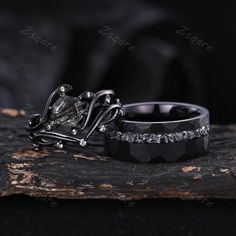 two wedding rings with black diamonds on them sitting on a piece of driftwood in the woods