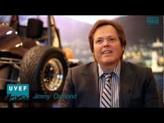 a man wearing a suit and tie sitting in front of a car with the words jimmy osmond on it