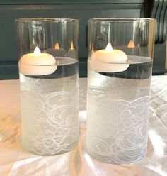 two clear glass vases with lit candles in them on a tablecloth covered surface