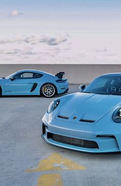 two blue sports cars parked next to each other in a parking lot with clouds in the background