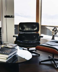 an eames chair and ottoman in front of a window with a book on it