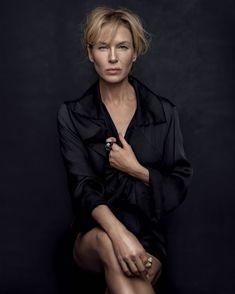 a woman sitting on top of a chair in front of a black background with her legs crossed