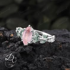 a pink stone ring sitting on top of a black rock with leaves and vines around it