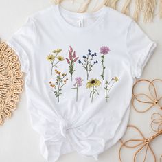 Unleash the vibrant spirit of nature with our Watercolor Flowers Shirt. This delightful wildflower shirt is a piece of wearable art, blending comfort and style with the beauty of the great outdoors. Each shirt features a stunning watercolor floral design, hand-painted with care to capture the intricate details and unique charm of wildflowers. From delicate petals to slender stems, every element in the design adds to the vibrant tableau, creating a look as refreshing as a walk through a meadow. M Multicolor Cotton Shirt With Plant Print, Nature-inspired Crew Neck T-shirt For Summer, Bohemian White T-shirt With Floral Embroidery, White Botanical Crew Neck Top, Nature-inspired Cotton T-shirt For Spring, Multicolor Crew Neck Shirt With Plant Print, Summer Birth Flower Short Sleeve T-shirt, White Bohemian T-shirt For Spring, Birth Flower Short Sleeve T-shirt For Summer