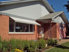 a brick house with an american flag in the window and flowers on the front lawn