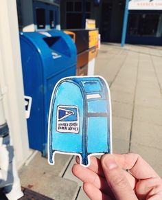 a hand holding up a blue mailbox sticker