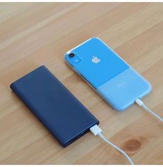 an iphone charging on a wooden table next to another cell phone with the battery plugged in