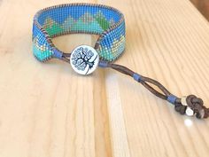 a bracelet with a tree on it sitting on top of a wooden table next to beads