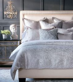 a bed with silver and white pillows in a bedroom next to a busturine