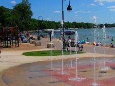 people are swimming and playing in the water at a park by the lake with fountains