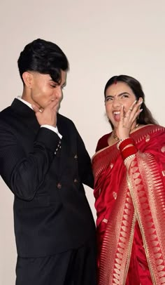 a man standing next to a woman in a red sari and holding her hand over her mouth