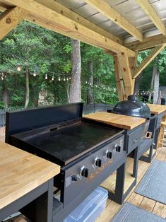 an outdoor bbq with grills and benches on the deck in front of trees