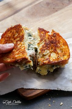 a person is holding up a grilled cheese and spinach sandwich on parchment paper