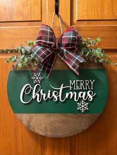 a merry christmas sign hanging on the front door with evergreen leaves and snowflakes