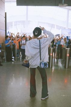 a woman standing in an airport with her back to the camera and arms raised up