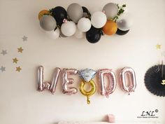 balloons are hanging on the wall above a crib that says we do in gold, silver and black