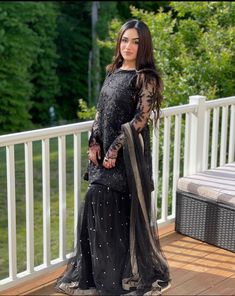 a woman standing on top of a wooden deck wearing a black dress with sheer sleeves