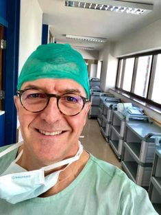 a man in scrubs is smiling for the camera while wearing glasses and a green hat