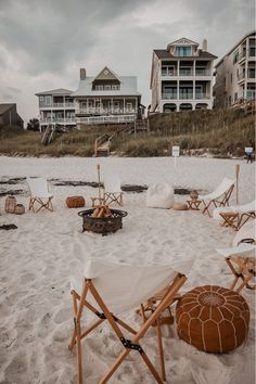 there are many lawn chairs on the beach with an umbrella and fire pit in the sand