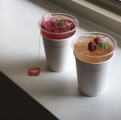 two plastic cups filled with drinks sitting on top of a counter next to a window