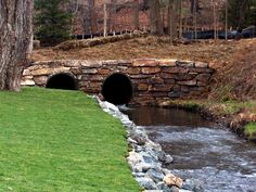 a small stone bridge over a stream in the middle of a field with grass and trees