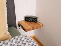 an alarm clock sitting on top of a wooden shelf next to a bed in a bedroom