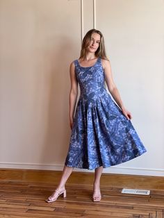 a woman in a blue dress standing on a hard wood floor next to a wall