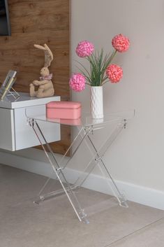 a white desk with pink flowers in a vase and a stuffed rabbit on the side