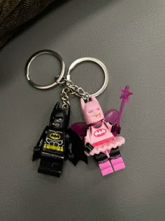 two lego batman keychains one is pink and the other is black with a batgirl on it