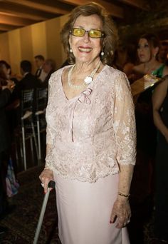 an older woman wearing glasses and holding a cane in front of a group of people