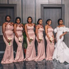 a group of women standing next to each other in front of a wall wearing pink dresses