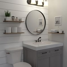 a white toilet sitting next to a bathroom sink under a round mirror on a wall