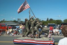 men in uniforms holding an american flag on top of a stone monument with people watching